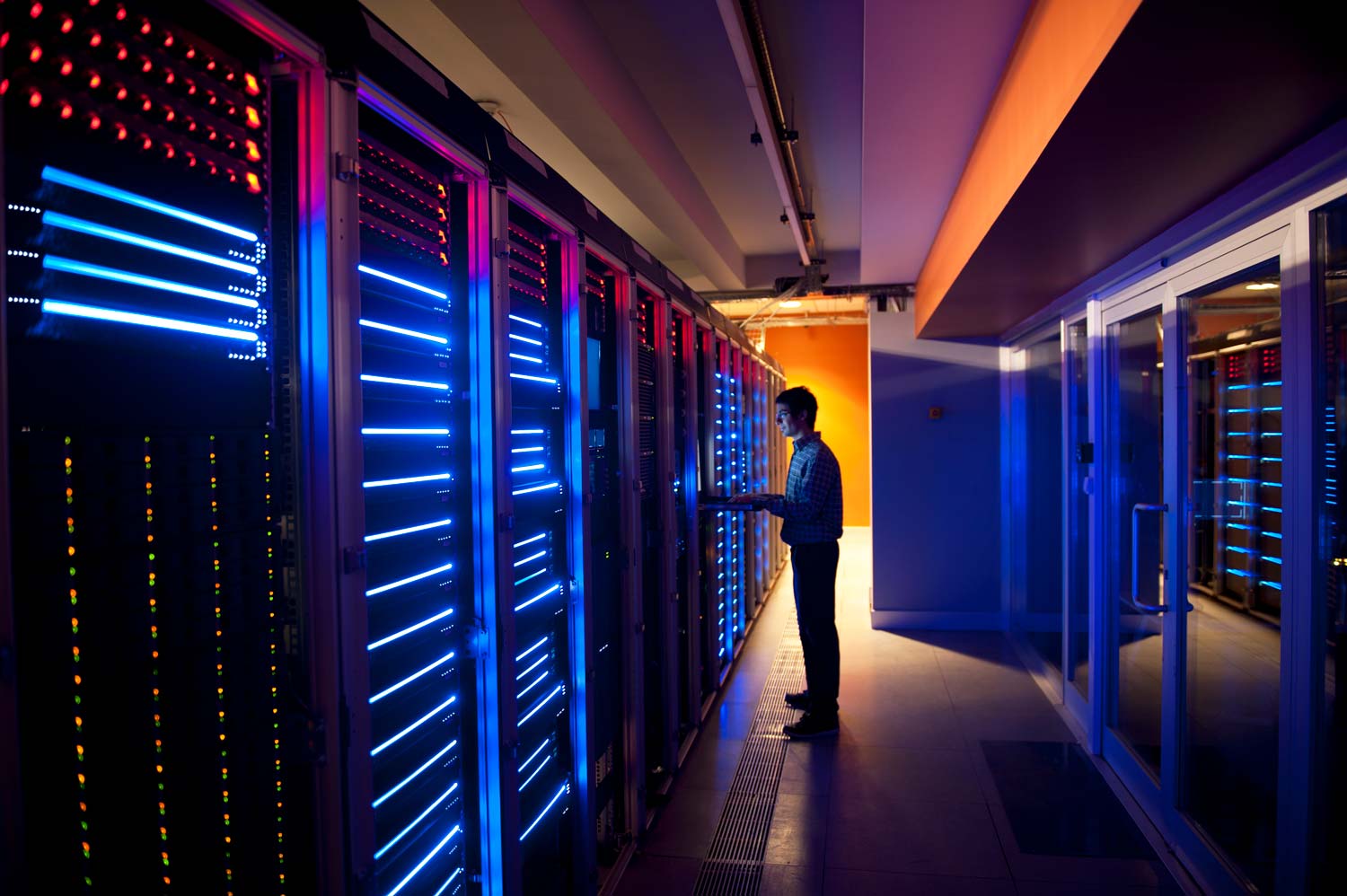 Eine Person steht in einem schmalen Gang eines Rechenzentrums und bedient ein Gerät an einem der blau leuchtenden Server-Racks.
